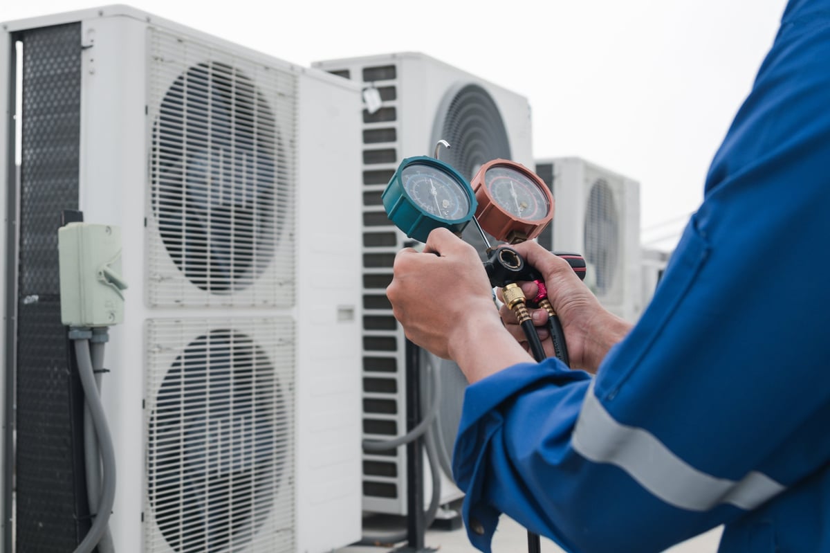 HVAC technician servicing an air conditioning unit with measurement equipment
