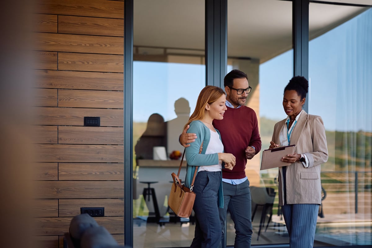 Two real estate agents with a buyer standing outside a beautiful new home
