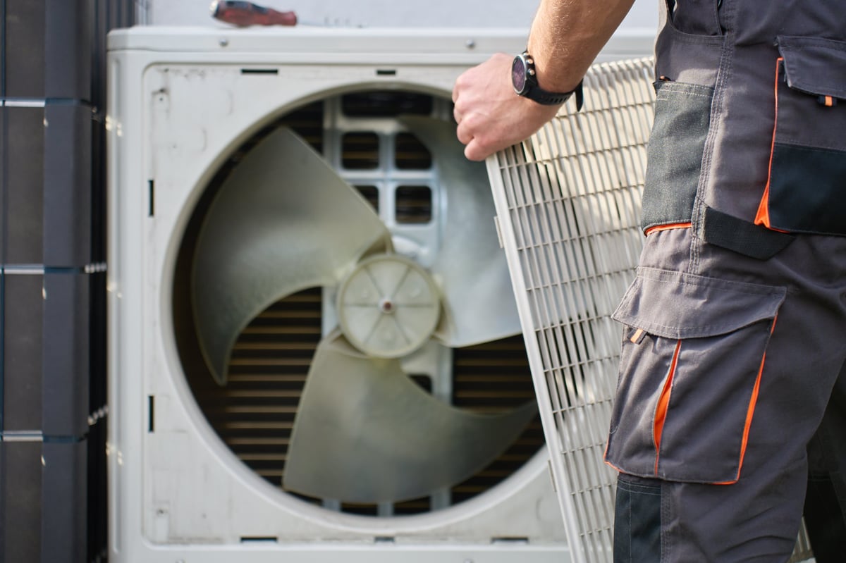 Technician opening the cover of a residential heat pump unit during HVAC service